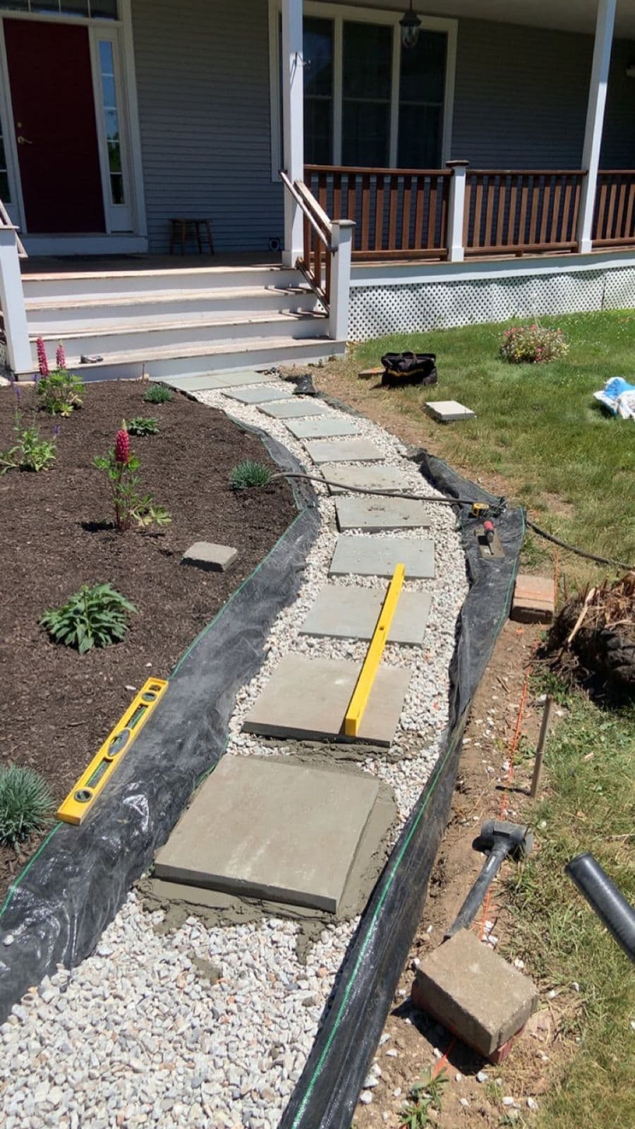 In-progress stepping stone path being set in gravel with a level and tools beside a porch