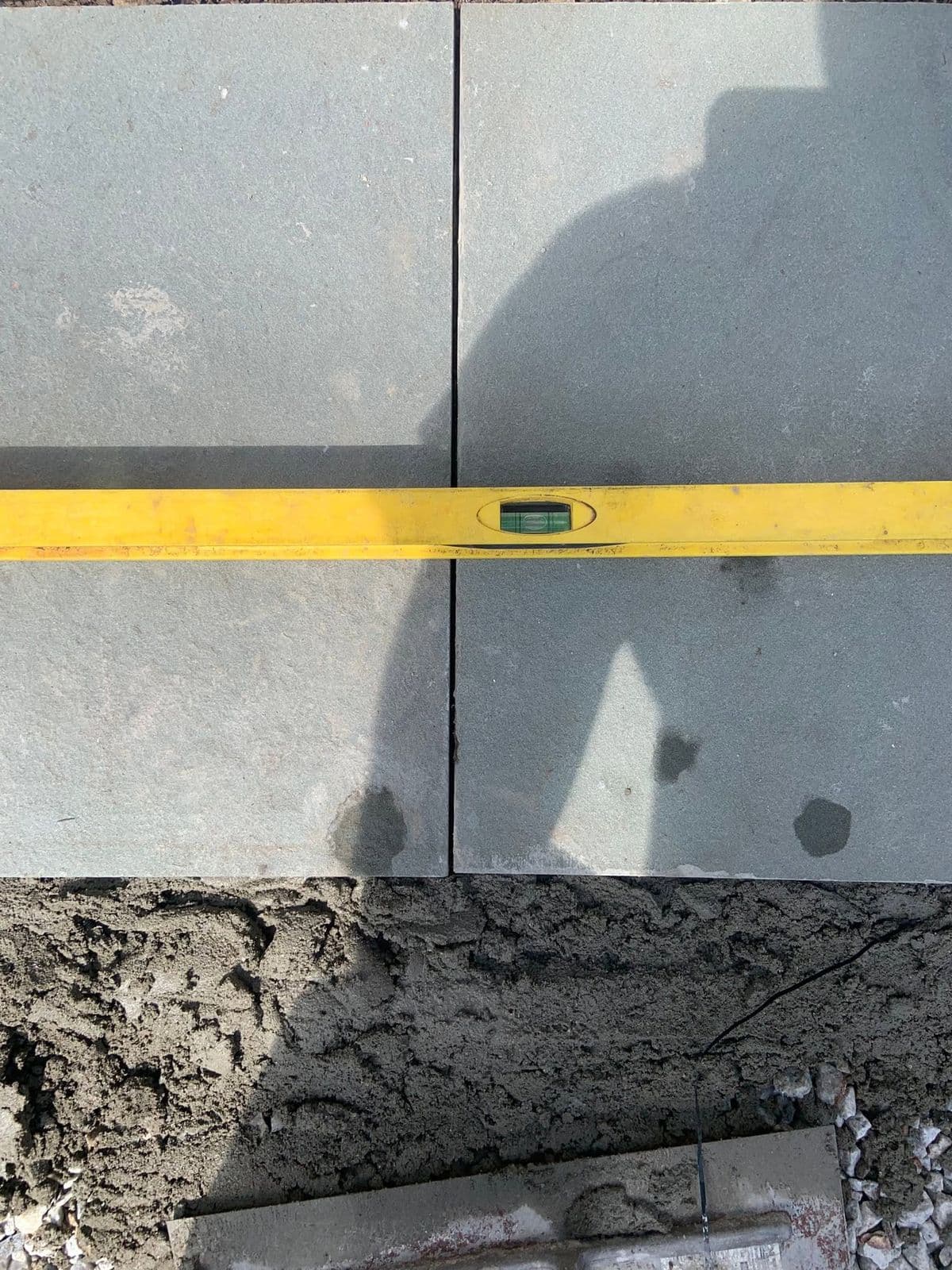 Close-up of a yellow level checking two gray bluestone pavers set in wet mortar