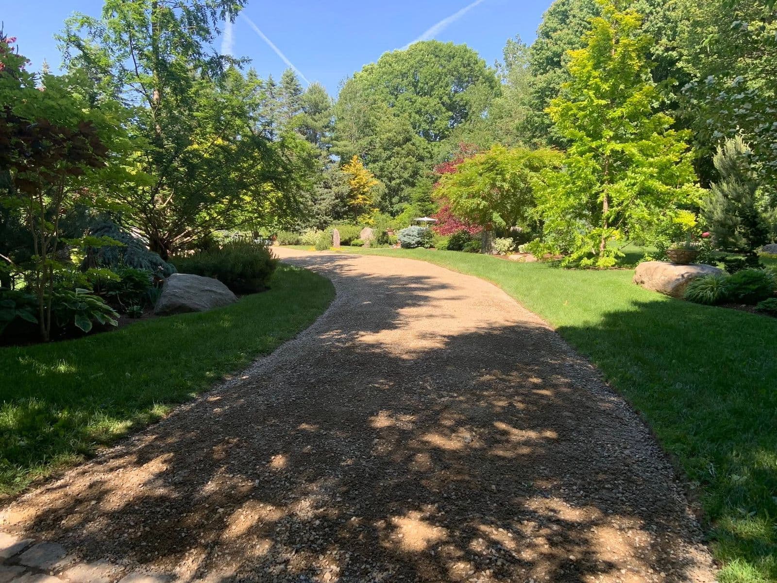 Curved gravel driveway winding between mowed lawns, garden beds, and mature trees