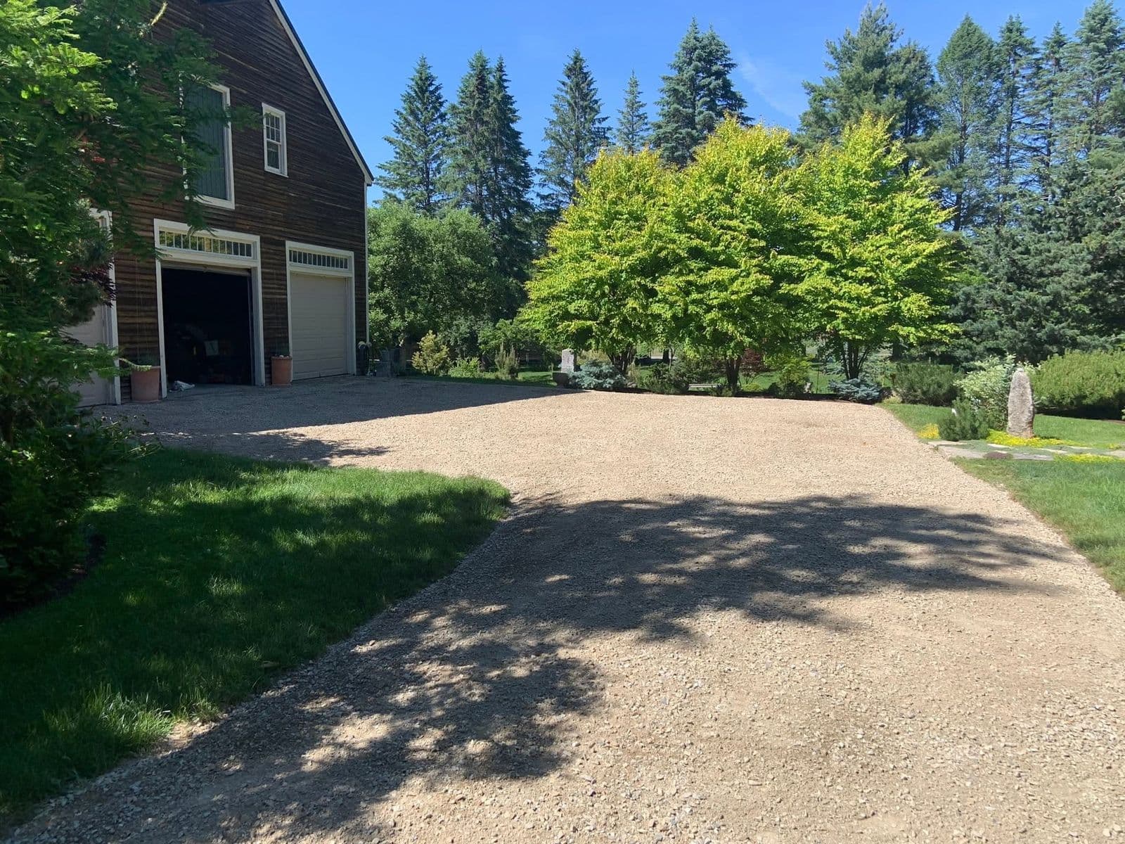 Fresh gravel driveway beside a dark wood barn with open garage doors