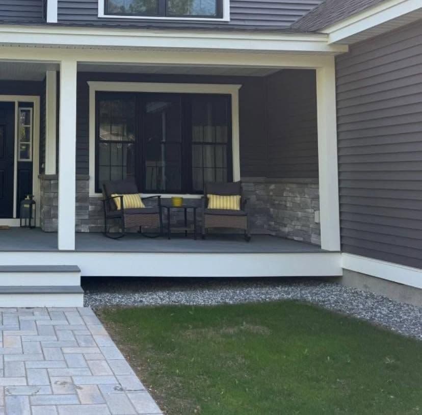 Covered porch with wicker chairs, stone veneer columns, gravel border and paver walkway