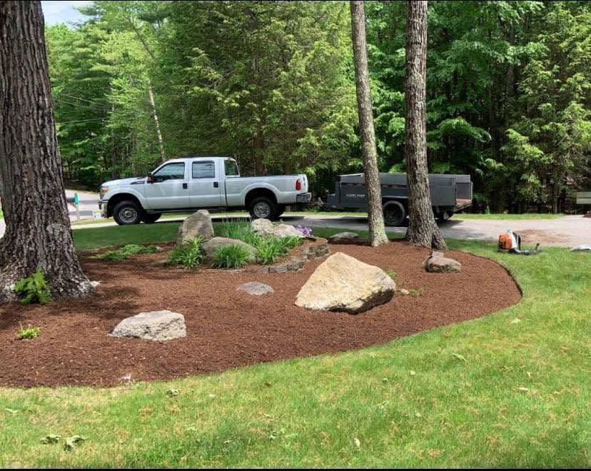 Brown mulch island bed with boulders and plantings, truck and trailer behind