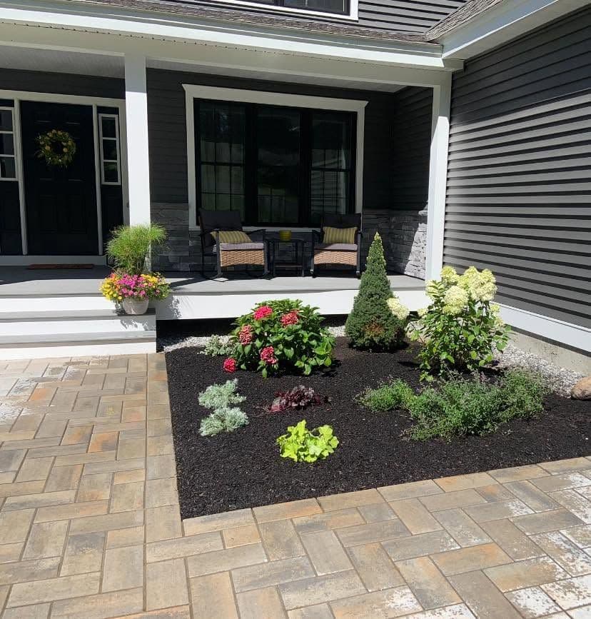 Black mulch bed with hydrangeas and shrubs bordered by a paver patio at a porch