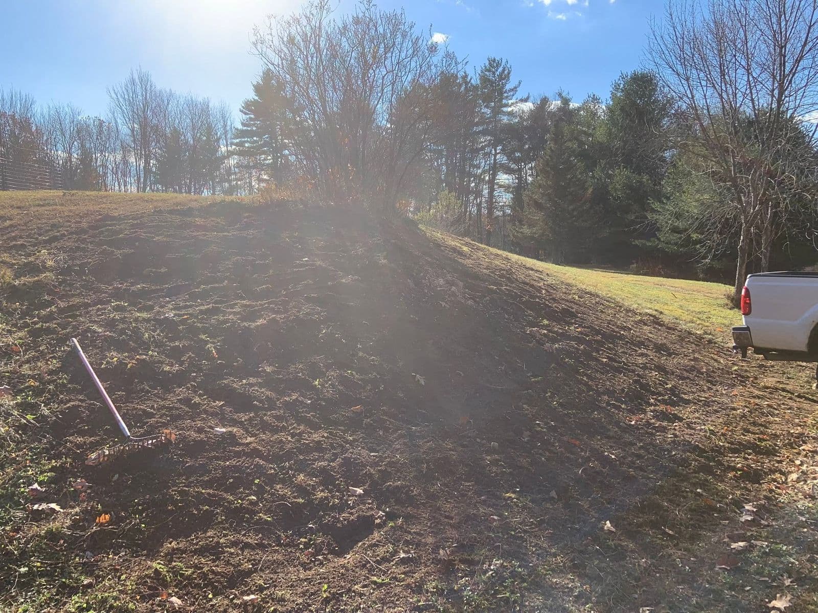 Freshly graded bare soil slope with a rake and a white pickup truck parked at right