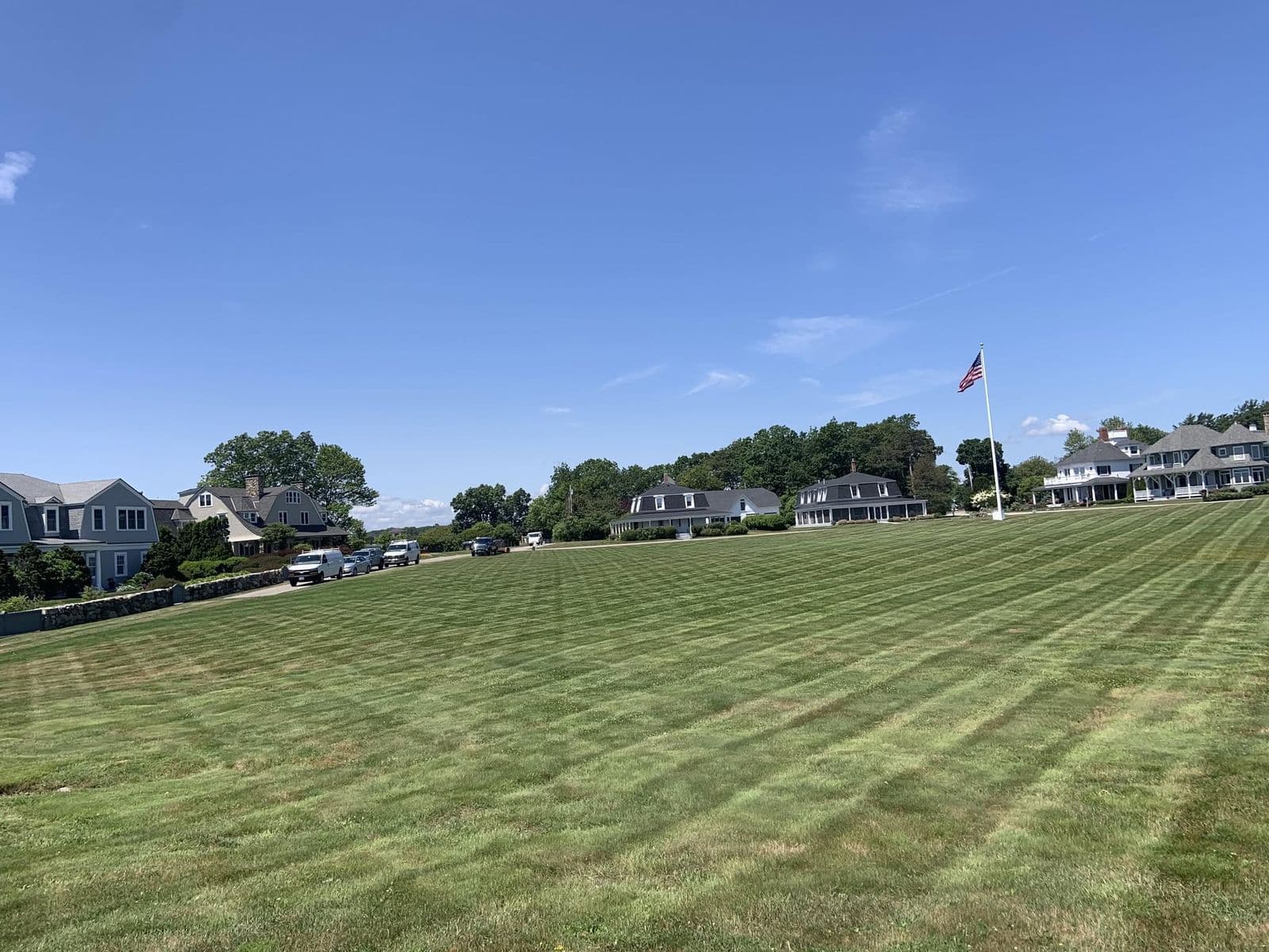 Large striped freshly mowed lawn with an American flag, shingled houses, and clear blue sky